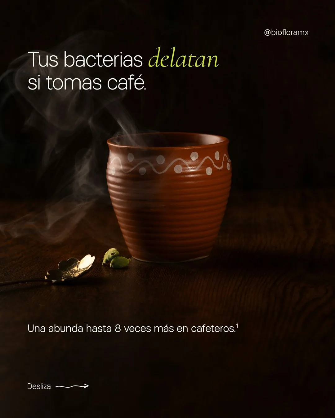 Un jarrito de barro humeante sobre una mesa de madera oscura, con cardamomo y una cuchara dorada, bajo el texto «Tus bacterias delatan si tomas café».