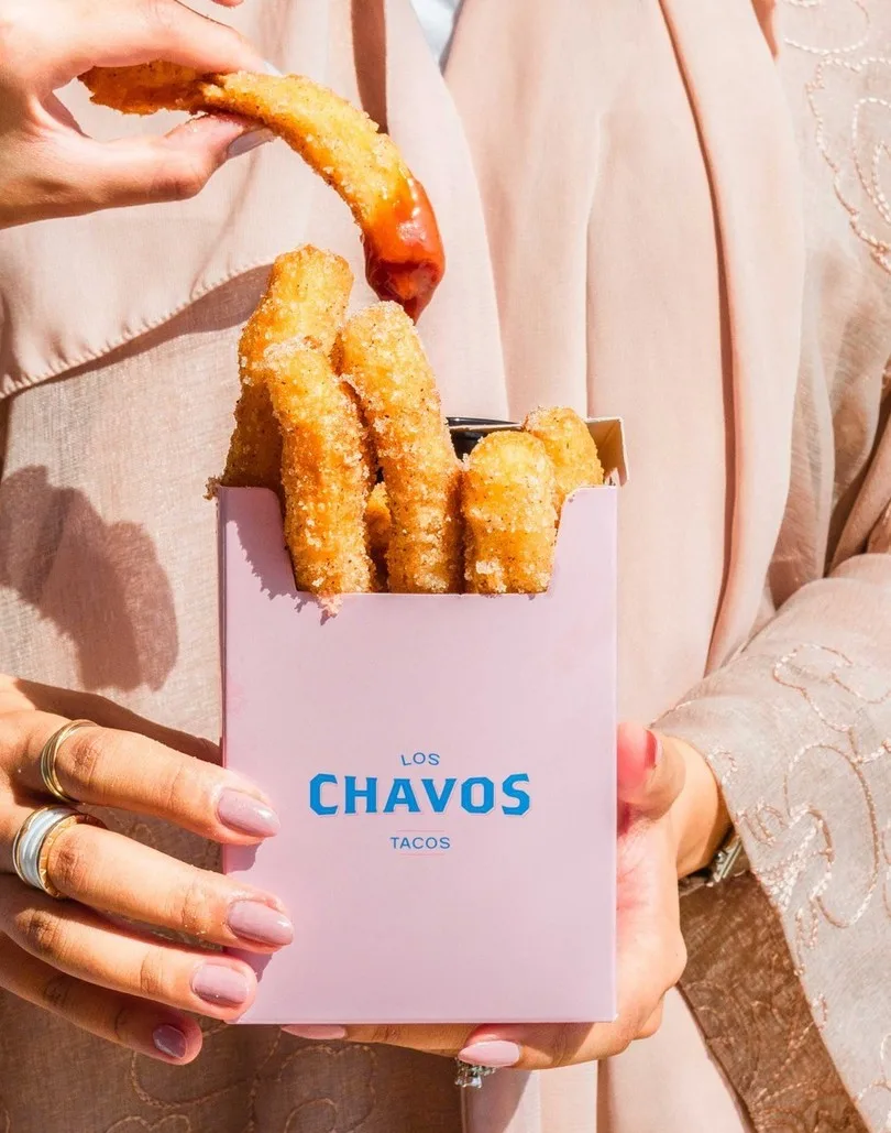 Caja rosa para churros con el logotipo en azul, en las manos de una persona.